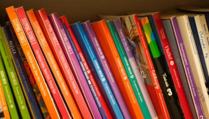 Oppikirjoja rivissä hyllyllä.