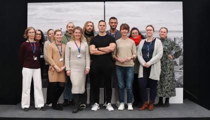 Kolmetoista henkilöä seisoo pienellä korokkeella. Taustalla ilmakuvaa Tampereen keskustasta.