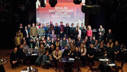 Suuri ryhmä ihmisiä poseeraa yhteiskuvassa. Taustalla valotaulu, jossa lukee "Nekalan kulttuurikeskus Nekalab avaa ovensa 1.1.2026".