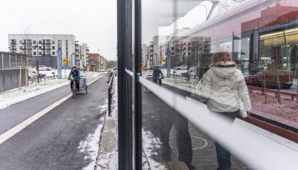 Pyöräilijä ja pyörän vetokärry lähestyvät ratikkapysäkkiä yhtä aikaa ratikan kanssa Hervannassa.