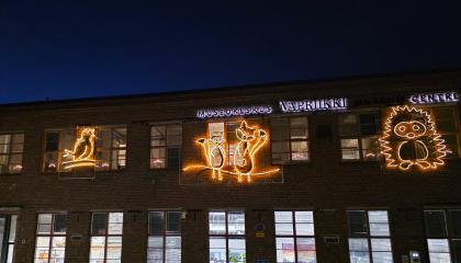 Vapriikin ulkoseinällä eläinvalohahmoja: lintu, kaksi kettua ja siili. Rakennuksen ikkunoista loistaa valoa pimeässä illassa.