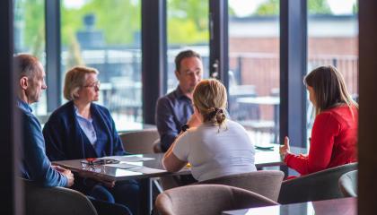 Kuvassa viisi henkilöä istuu pöydän ääressä.