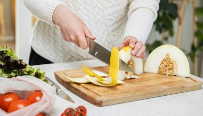 Ruonlaittaja leikkaa hunajamelonia. Pöydällä on myös tomaatteja ja salaattia.