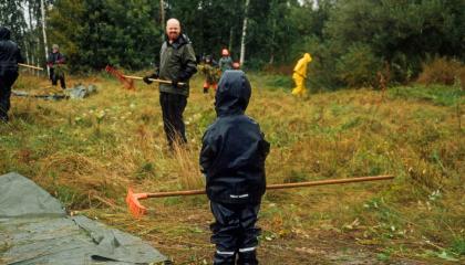 Aikuinen, lapsi ja muuta väkeä haravoimassa niittytalkoissa.