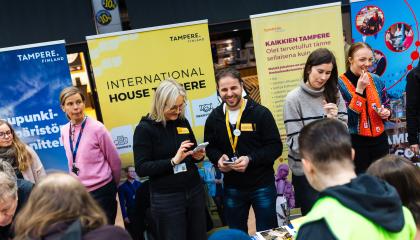 Useita hymyileviä kaupungin työntekijöitä asukasillan esittelypisteillä. Heidän takanaan on värikkäitä roll-upeja.