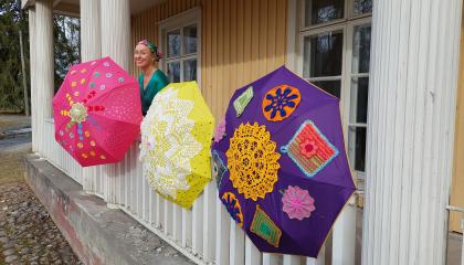 Kartanon ulkokaiteeseen on kiinnitetty kirjavia ja pitsein koristeltuja sateenvarjoja.