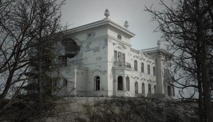 Milavidan valkoinen palatsi pommitusten jäljiltä, edessä lehdettömiä puita.