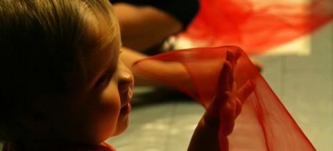The baby is waving a red circus scarf.