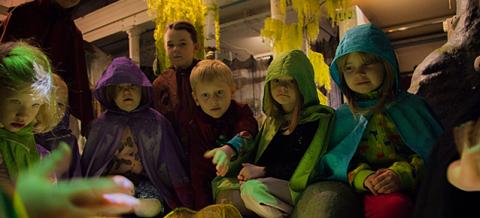 The children sit around a green play pond dressed as forest dwellers.