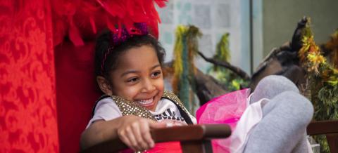 Child sits on a red chair and laughs.