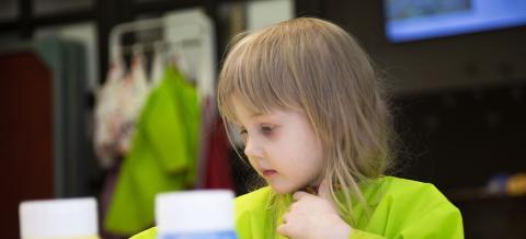 Takaa-alalla lapsi viChild wearing a green apron, and in front of her yellow and blue paintcan. 