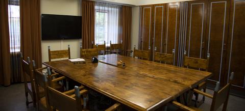 The conference room is filled with dark wood furniture. A large table in the centre of the room is surrounded by chairs.