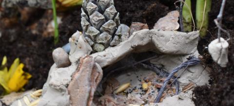 Eskarilaisen savesta, siemenistä ja kävystä tekemä ympäristöteos narsissien juurella.