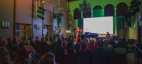 A violinist and pianist perform in a concert hall to a full audience.
