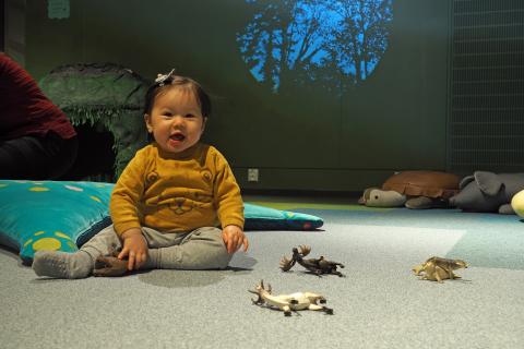Taapero istumassa Rullan elämystilan lattialLittle child sitting on Rulla's Terra-space with little plastic animal toys.