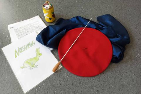 Kapellimestarin tahtipuikko, punainen baskeri, sininen huivi, askarreltu tölkkihelistin ja ohjepapereita.