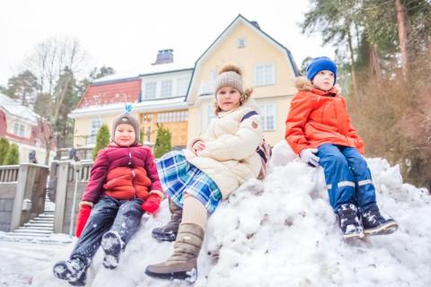 Kolme lasta istuvat lumipenkassa.