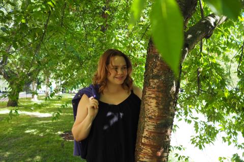 Nuori punatukkainen nainen seisoo vihreässä maisemassa ja hymyilee. 