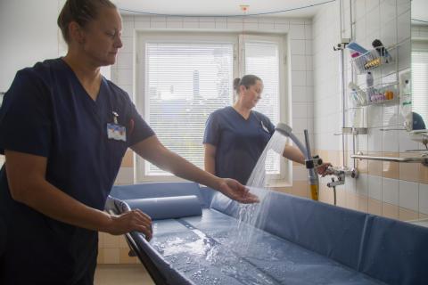 Lähihoitajat testaavat suihkuveden lämpötilaa kädellä kokeillen.