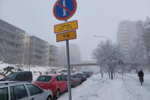 Etualalla vuoropysälöintimerkki ja kadun varrella pysäköityjä autoja, taustalla kerrostaloja.
