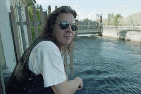 Pate Mustajärvi katsoo kameraan aurinkolasit päässään, taustalla Tammerkoski.