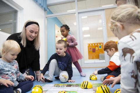 Varhaiskasvatuksen opettaja istuu lasten kanssa lattialla pelaamassa.