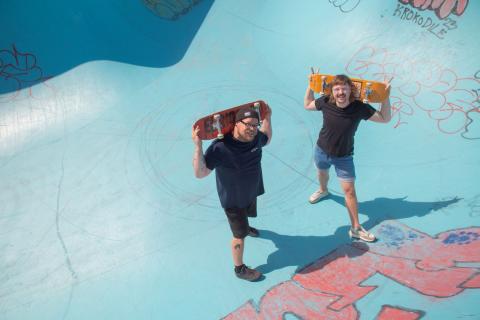 Kaksi nuoriso-ohjaajaa seisoo skeittialtaassa skeittilaudat olkapäillä.