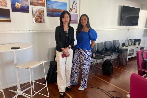 Kaksi naista seisovat vierekkäin kokoustilassa ja hymyilevät. 