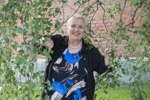 Henkilö katsoo koivun lehtien alta kohti kameraa.