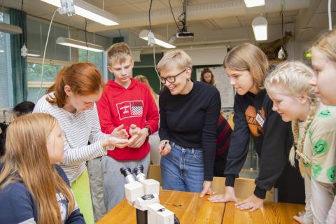 Students and a teacher are standing inside and studying water samples.