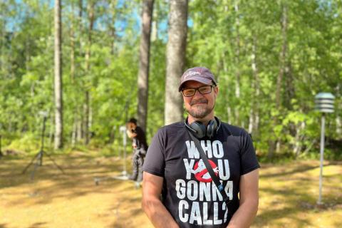 Ohjaaja Tommi Lepola seisoo kuvassa vehreä maisema taustalla.