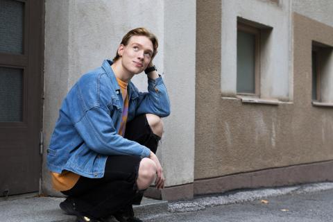 Oliver Priimägi squats down on a street corner and looks up smiling.