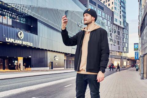 A man standing on the street in front of the Nokia Arena with a mobile phone in his hand.
