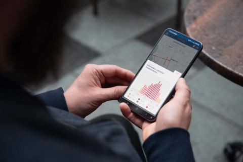 Hands holding a mobile phone with a screen showing a view of the Tampere Pulse tool.