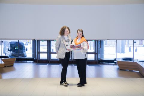 Two people are standing in the spacious lobby of the Workers' College, looking at papers.