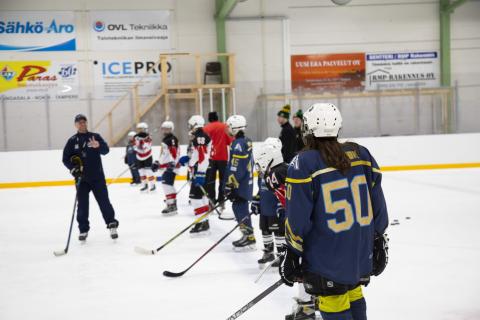 Nuoret jääkiekkoilijat jäällä valmentajansa kanssa.