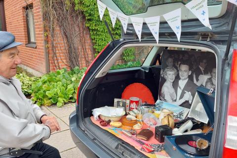 Harmaatakkinen mies katselee auton tavaratilaan aseteltua Peräkonttimuseon näyttelyä.