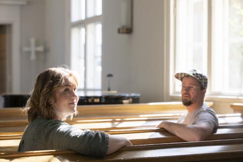 Nainen ja mies istumassa penkillä sisätiloissa.