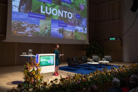Kaisa in a green dress and red shoes on the stage at the Nature Forum.