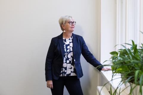 Kirsi Viskari seisoo porraskäytävässä ikkunasta ulos katsoen.