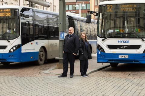 Kaksi bussikuskia seisoo hymyillen selät vastakkain kahden Nysse-bussin välissä.