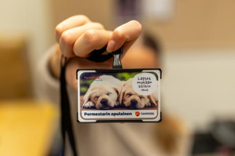Lähikuva kaulaan ripustettavasta henkilökortista, jossa on kuva kahdesta nukkuvasta koirasta. Tekstissä lukee "Pormestarin apulainen".