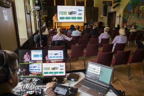 In the hall, people watch the performance on a big screen and a technician describes it on a webcast.
