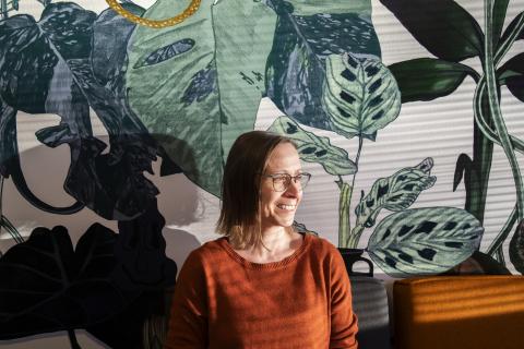 Silmälasipäinen henkilö katsoo sivulle. Takana on lehtikuvioinen verho.