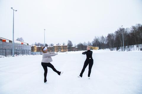 Kaksi vauhdikasta luistelijaa on toinen jalka ojennettuna luistelemassa vastakkain kasvot toisiinsa päin.