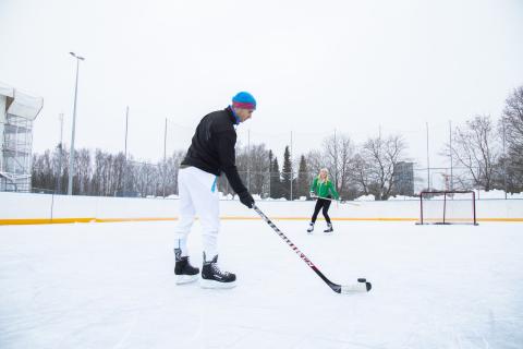 Etualalla seisova pelaaja on syöttämässä kiekkoa maalin lähellä seisovalle toiselle pelaajalle.