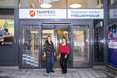 Kaksi henkilöä seisoo ulko-ovilla, joiden yläpuolella on Tampereen vaakuna ja lukee Tampere, työ ja yrittäminen sekä Tampereen seudun työllisyysalue.