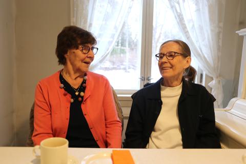 Kaksi henkilöä istuvat ja juttelevat pöydän ääressä.