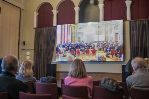 People watch the Council’s anniversary broadcast on a wall screen.