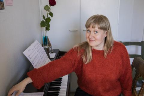 Kielo-Kristiina Kärkkäinen istuu tuolilla ja nojaa pianoon.